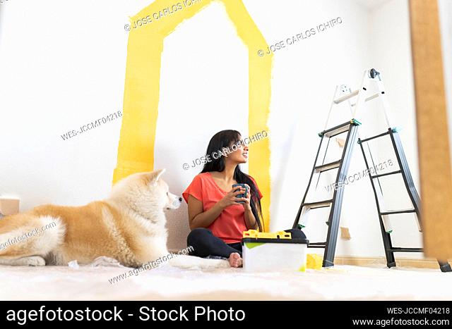 Smiling young woman having coffee by Akita dog at home