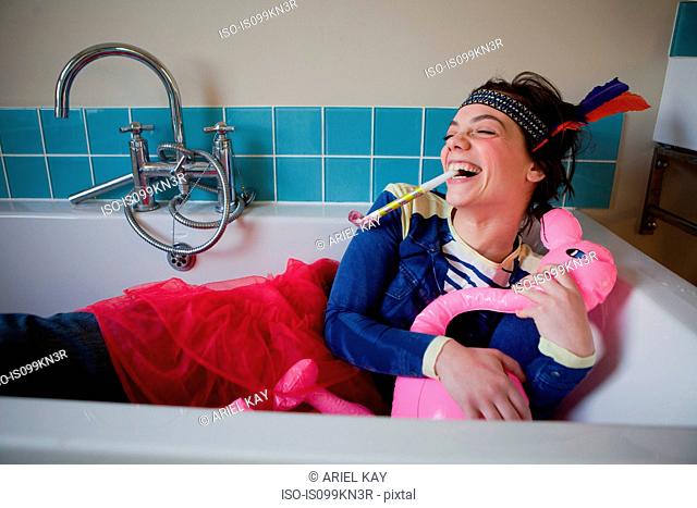 Young woman in bath, wearing costume and blowing party blower