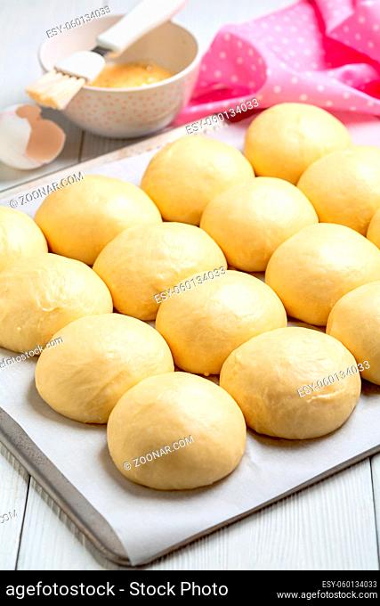 Place the homemade sweet yeast buns on a parchment-lined baking sheet. Concept of home baking