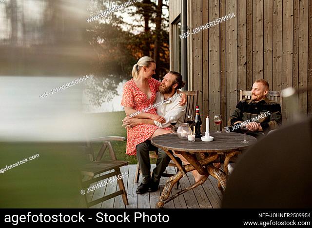Couple with friend sitting on patio and drinking wine