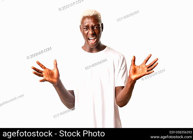 Portrait of angry and pissed-off african-american blond man, shaking hands and screaming outraged, standing over white background mad