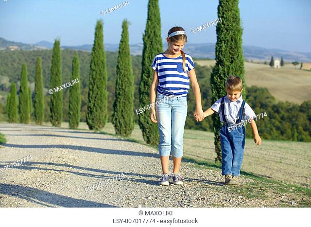 Happy sister and brother having fun on vacations in Tuscan against cypress alley background