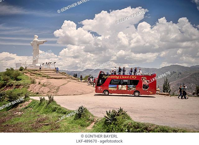 Red Tourist Bus stopping at the viewing platform of the white Christ Statue with view to the surrounding Andes Cuzco, Peru, Sout
