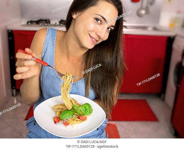 young woman eating wholemeal spaghetti with tomatoes and basil