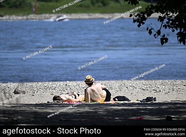 04 June 2023, North Rhine-Westphalia, Rodenkirchen: A couple lies on the beach of the Rhine and enjoys the warm weather with sunshine to cool off in the cool...
