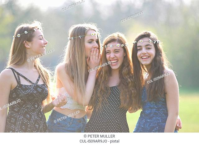 Four teenage girls wearing daisy chain headdresses giggling in park