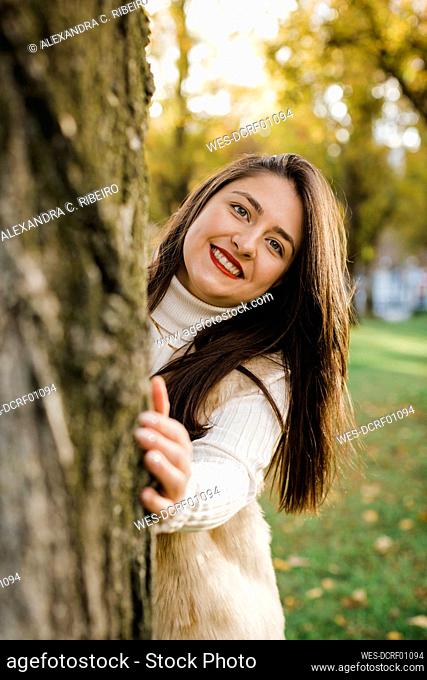 Happy woman with long hair standing by tree in public park