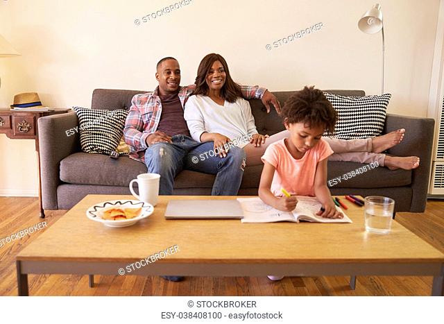 Parents Watch TV As Daughter Colors In Picture Book