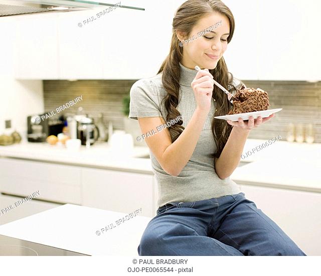 Woman eating chocolate cake in kitchen