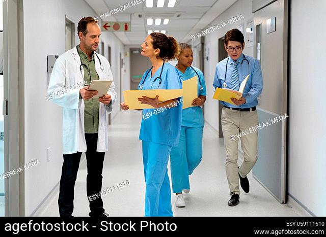 Diverse group of male and female doctors walking through corridor discussing