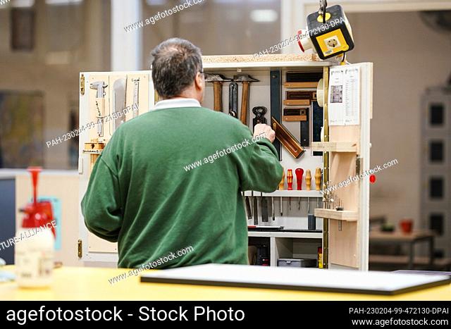 PRODUCTION - 03 February 2023, Baden-Württemberg, Bruchsal: An inmate takes a tool from a cupboard in the carpentry workshop at Bruchsal Prison