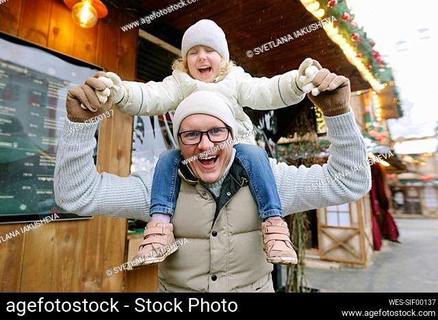 Happy father carrying daughter on shoulders at Christmas market