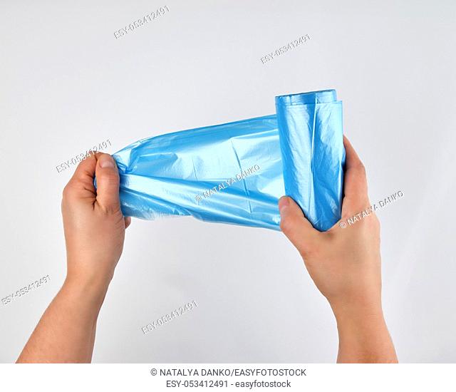 blue plastic trash bag in his hands on a white background, a man tears one from a roll