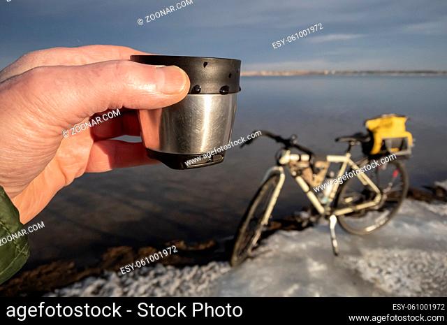 cup of hot tea on an icy lake shore during winter biking, Boyd Lake State Park in northern Colorado