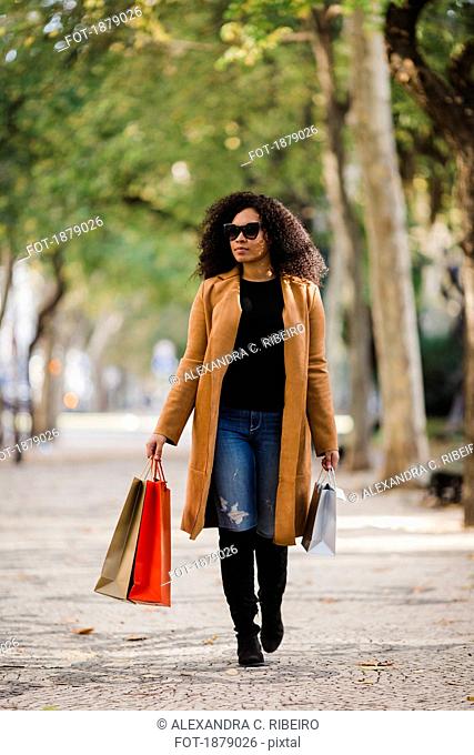 Stylish young woman walking with shopping bags on sidewalk