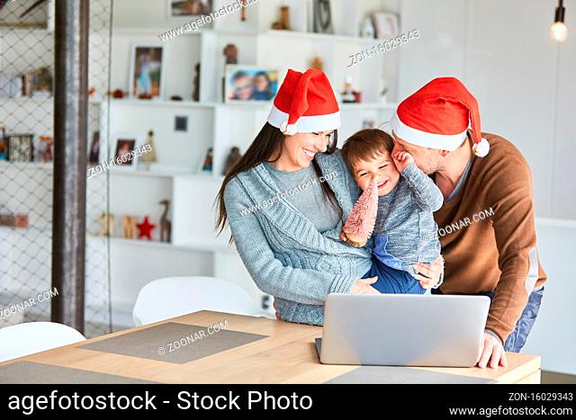 Familie mit Kind auf dem Arm macht Videochat oder Videoanruf zu Weihnachten im Wohnzimmer zu Hause