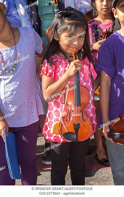 Proudly holding her violin, a smiling Hispanic girl poses with fellow musicians at a Santa Ana, CA, community center