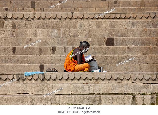 Hindu Sadhu holy man with traditional robe reads on steps of the Ghats in holy city of Varanasi, Benares, Northern India