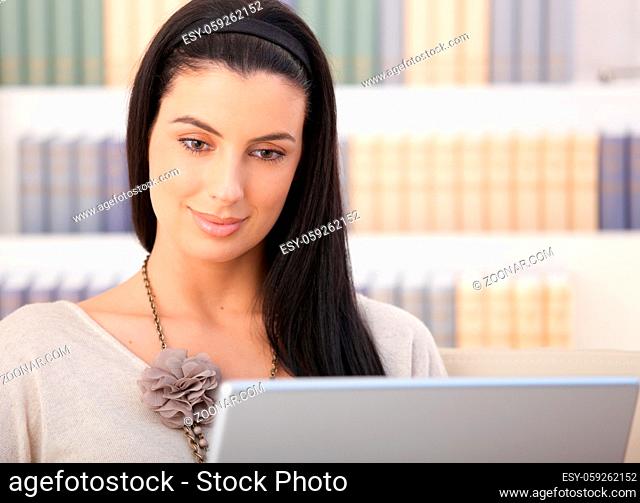 Closeup portrait of smiling woman looking at laptop computer screen at home