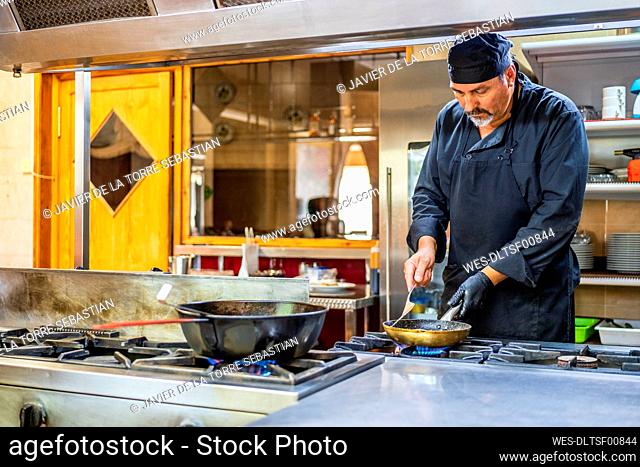 Chef with pan in traditional Spanish restaurant kitchen