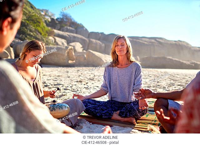 Serene woman meditating in circle on sunny beach during yoga retreat