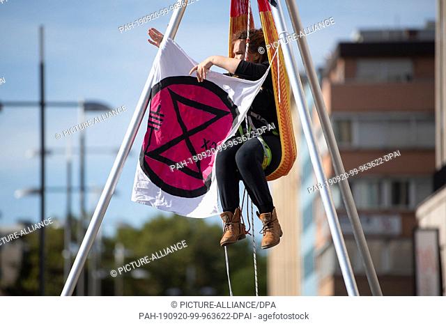 20 September 2019, Baden-Wuerttemberg, Stuttgart: An activist sits on a street in downtown Stuttgart in a hammock attached to a tripod and has a flag with the...