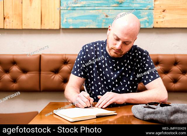 Mid adult man writing in notebook while sitting in cafe