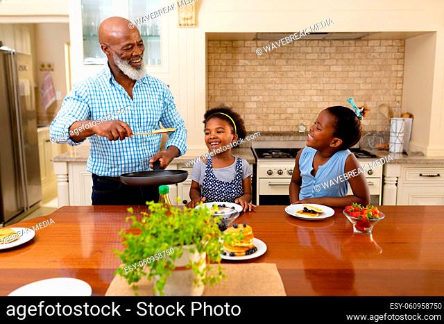 African american grandfather serving breakfast for his two granddaughters in the kitchen at home