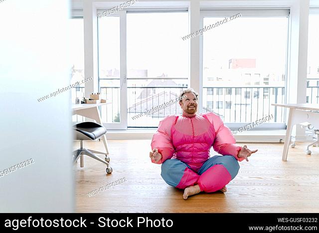 Businessman in office wearing pink bodybuilder costume practicing yoga