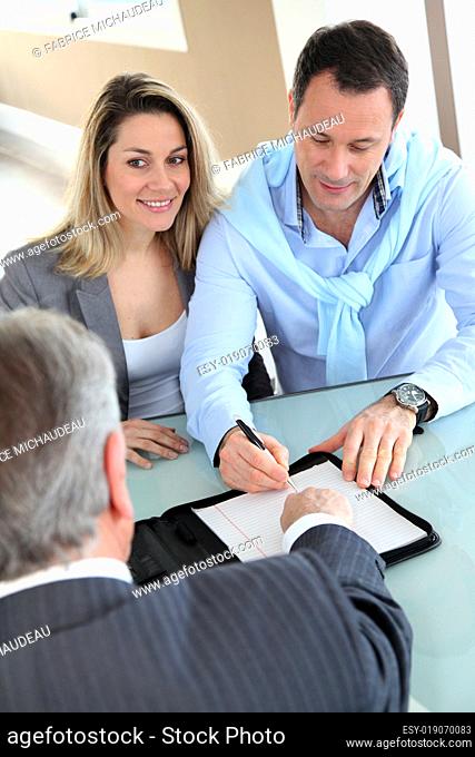 Happy couple signing purchase contract with real-estate-agent