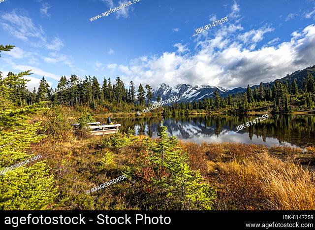 Hikers at a viewpoint, Mt. Shuksan glacier with snow reflecting in Picture Lake, forested mountain landscape in autumn, Mt