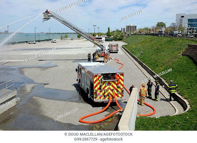 A fireman in a bucket aims a hose on a cement area of a public plaza while other fireman watch during a maintenance procedure at the Festival Plaza in Windsor