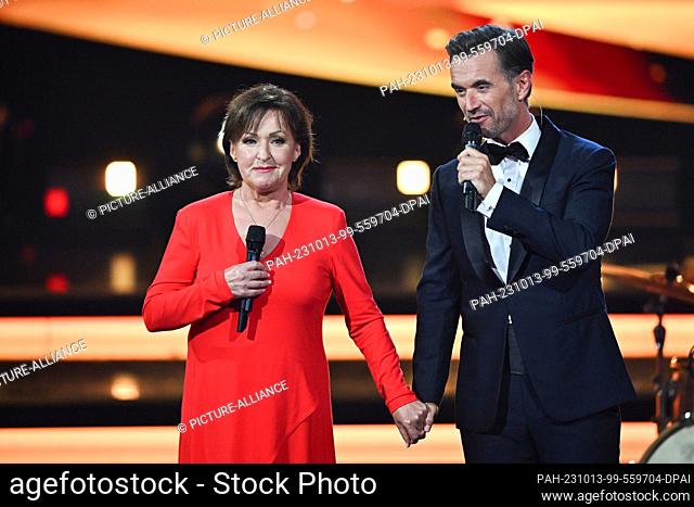 13 October 2023, Saxony, Leipzig: Singer Ute Freudenberg stands hand in hand next to presenter Florian Silbereisen on stage at the ""Goldene Henne"" media award...