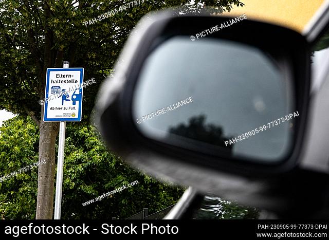 01 September 2023, Lower Saxony, Northeim: A ""parent stop"" sign stands behind a car's rearview mirror at Martin Luther Elementary School