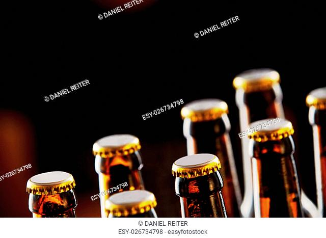 Two rows of unopened brown beer bottles in a closeup diagonal view over a dark background with copy space