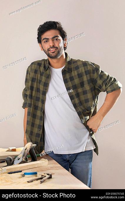 A YOUNG CARPENTER LOOKING AT CAMERA AND SMILING WHILE WORKING