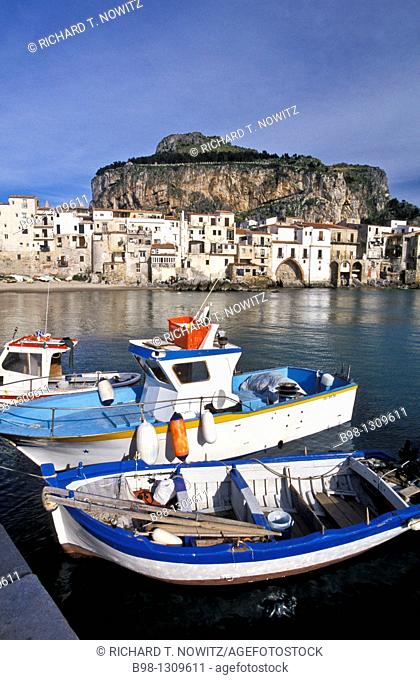 Cefalu, Sicily, Italy  Fishing harbor of the medieval town in late afternoon light  Boats tied to dock  Village and giant rock 'la rocca' in background...