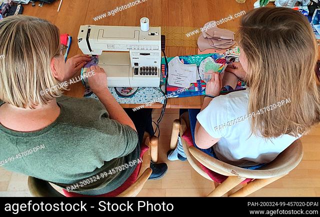 HANDOUT - 24 March 2020, ---: Caroline Maier (r) sews together with her mother face mask out of three layers of cheerfully patterned cotton fabric