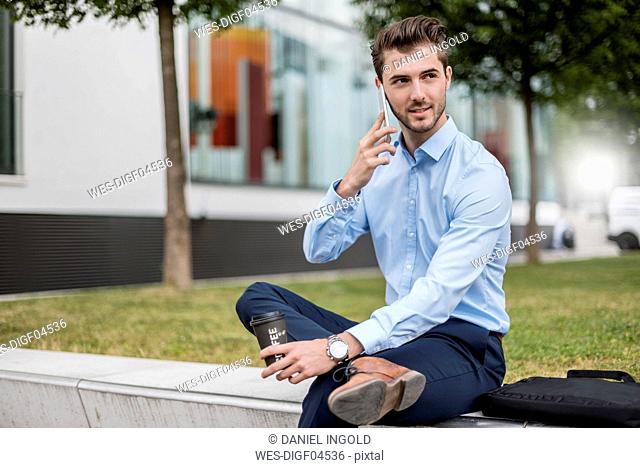 Smiling businessman sitting outdoors with cell phone and takeaway coffee
