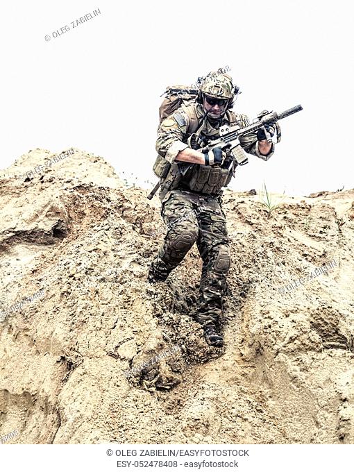 United States army commando, special forces infantry armed with assault rifle in combat uniform and load carrier, descending from steep sand dune