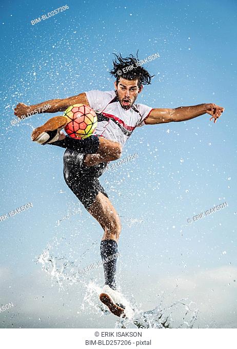 Water spraying on Hispanic man kicking soccer ball