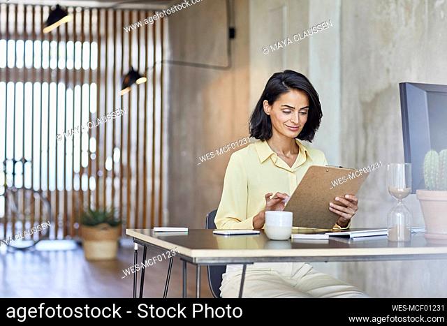Businesswoman holding clipboard while working at desk in office