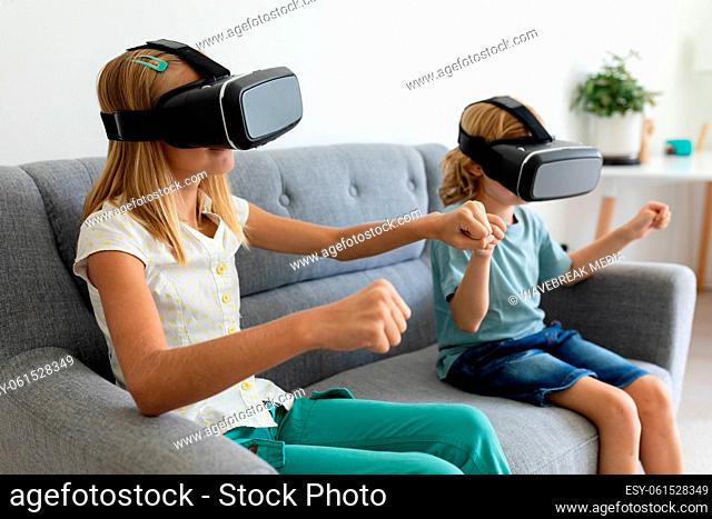 Caucasian brother and sister wearing vr headsets sitting on couch holding hands