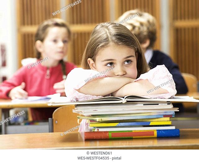 Girl sitting at school desk, leaning on stack of books