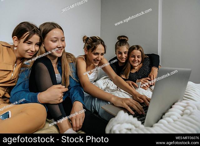 Group of girlfriends sitting on bed, watching movie on laptop
