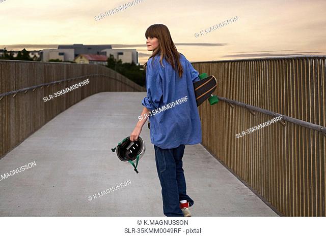Girl carrying skateboard on walkway