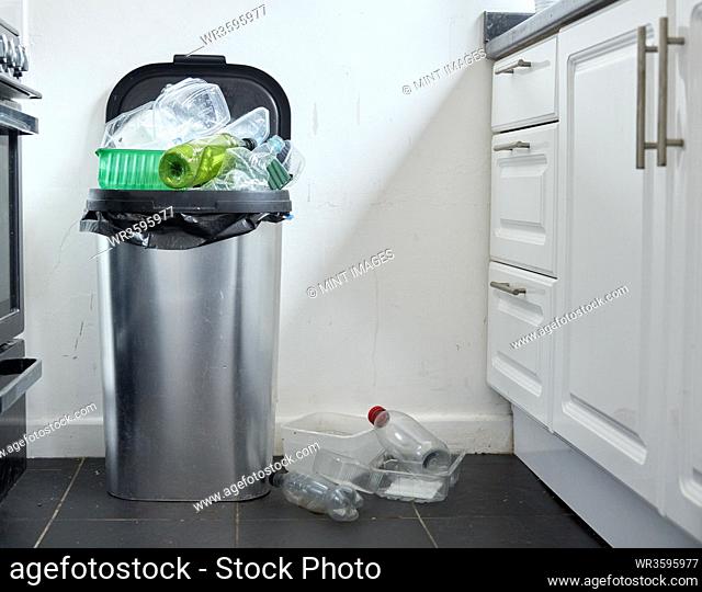 Various used plastic containers overflowing from dustin in kitchen