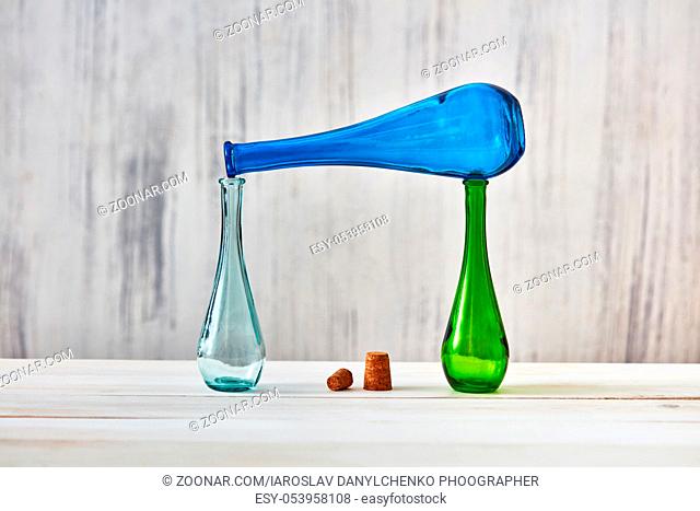 Two glass bottles stand on a table, a blue bottle lies on top of them with with corks on a light gray background. Concept of saving homemade products