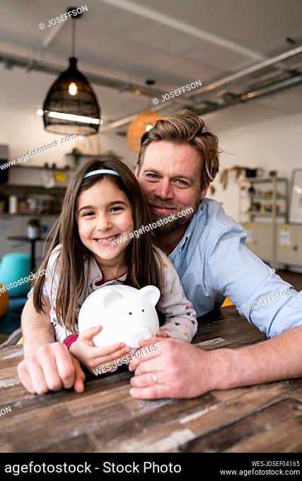 Smiling father and daughter with piggy bank at home