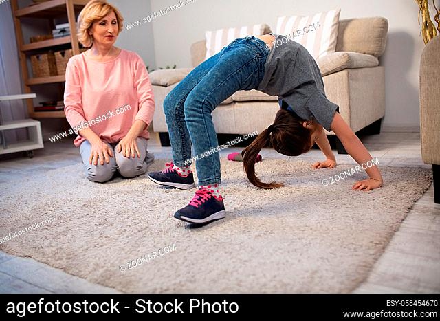 little girl making bridge on floor and her granny looking at her. Sport concept